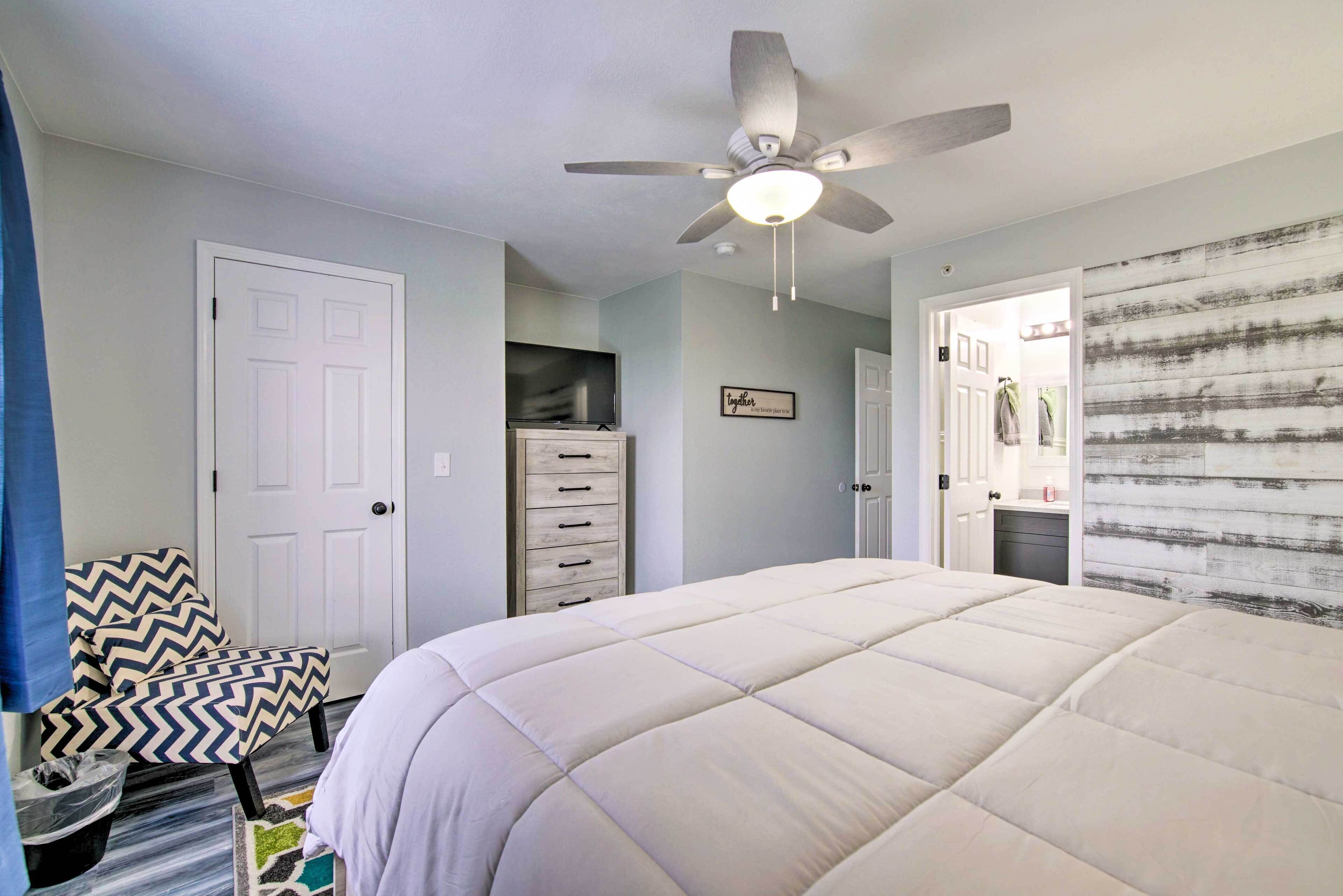 A bedroom with a bed, a ceiling fan, a dresser, a chair, and a door.