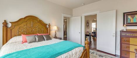 A bedroom with a wooden headboard, a bed with a teal blanket, a nightstand with a lamp, a dresser, and a ceiling fan.
