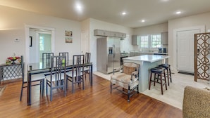Una cocina moderna con una isla central, una zona de comedor con una mesa de vidrio y un espacio de estar con un sillón estampado.