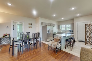 A modern kitchen with a central island, a dining area with a glass table, and a living space with a patterned armchair. - Walk to Amphitheater, Bjcc & Stadium: 1920s Gem! (Birmingham)