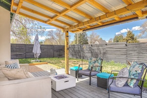 A covered outdoor patio with a wooden deck, outdoor furniture, and a fire pit.