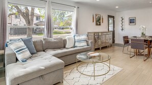A living room with a sectional sofa, a glass coffee table, and a dining area with a table and chairs. - 2 Mi to Cherry Creek Trail! Family Home w/ Patio (Denver)