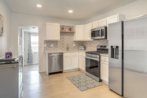 A modern kitchen with white cabinets, stainless steel appliances, and a patterned backsplash.