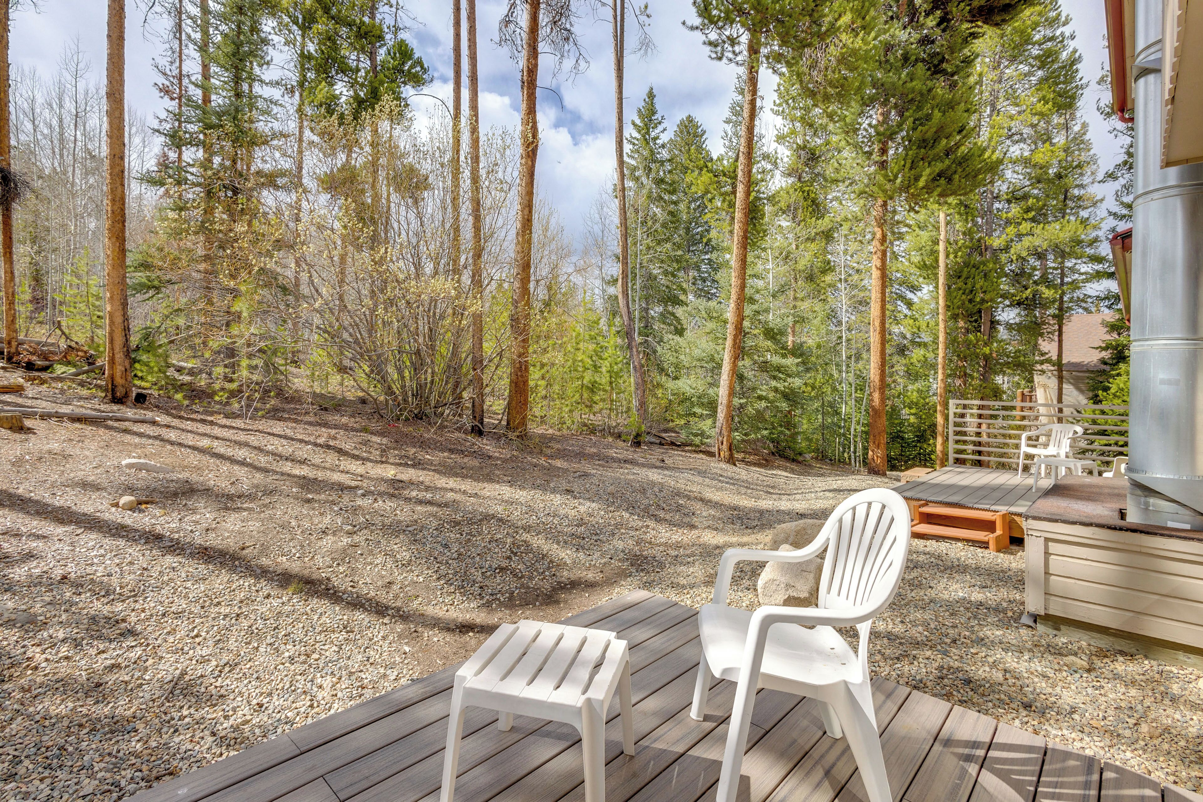A deck with two white chairs, a grill, and a view of a forest.