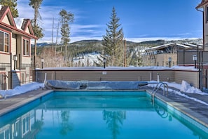 A swimming pool with a view of snow-covered mountains and pine trees. - Walk to Trails & Hideaway Park! Main Street Condo (Winter Park)
