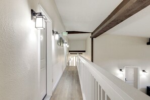 A hallway with white walls, a wooden ceiling beam, and a white railing. - Walk to Trails & Hideaway Park! Main Street Condo (Winter Park)