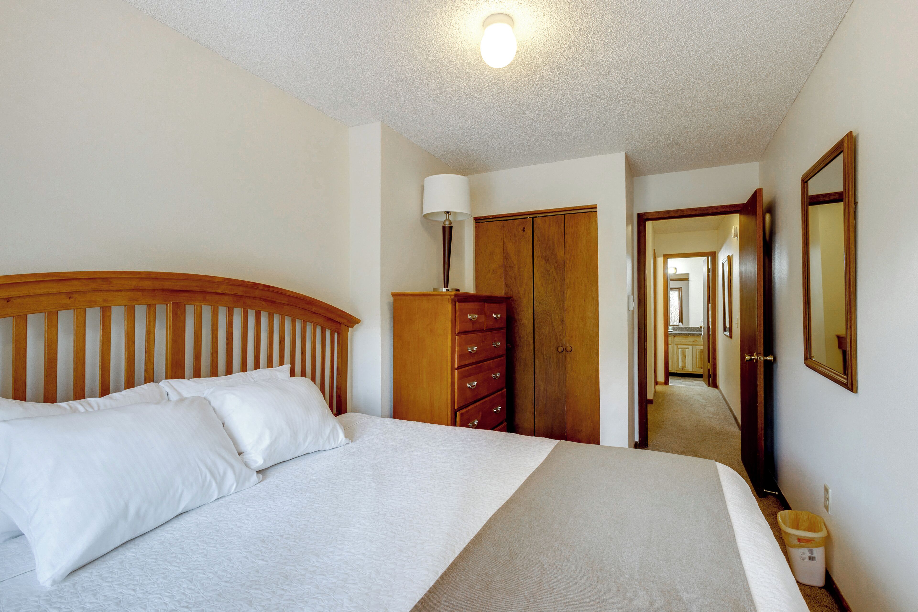 A bedroom with a bed, wooden wardrobe, and a hallway leading to a kitchen.