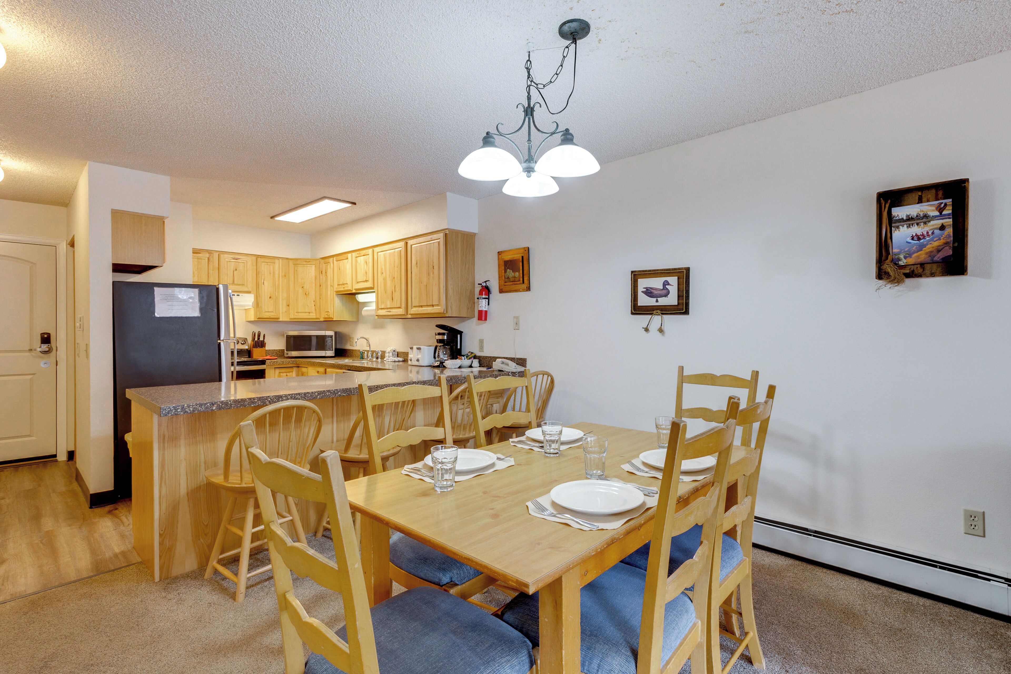 A kitchen with wooden cabinets, a refrigerator, a microwave, and a dining area with chairs and a table set for two.