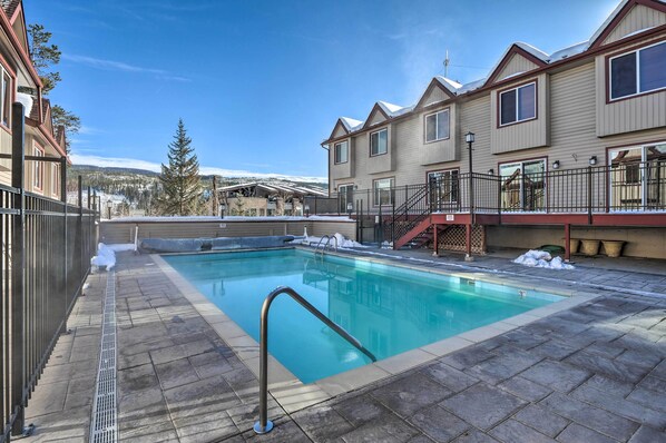 A swimming pool with a metal ladder, surrounded by a stone deck, and adjacent to a building with a balcony. - Walk to Trails & Hideaway Park! Main Street Condo (Winter Park)