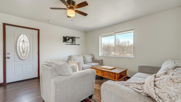 A living room with a ceiling fan, a sofa, a coffee table, and a window with a view of trees. - Alaskan Adventure Base 2 Mi to Dtwn Wasilla (Wasilla)