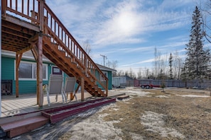 A residential property with a wooden staircase leading to a deck, a covered patio, and a fenced yard.