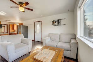 A living room with two sofas, a coffee table, a ceiling fan, a door with a decorative glass panel, and a kitchen area in the background. - Alaskan Adventure Base 2 Mi to Dtwn Wasilla (Wasilla)