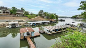 A marina with docked boats, a small building with a red roof, and houses in the background. - Dock + Swim Platform! Osage Beach Waterfront Home (Osage Beach)