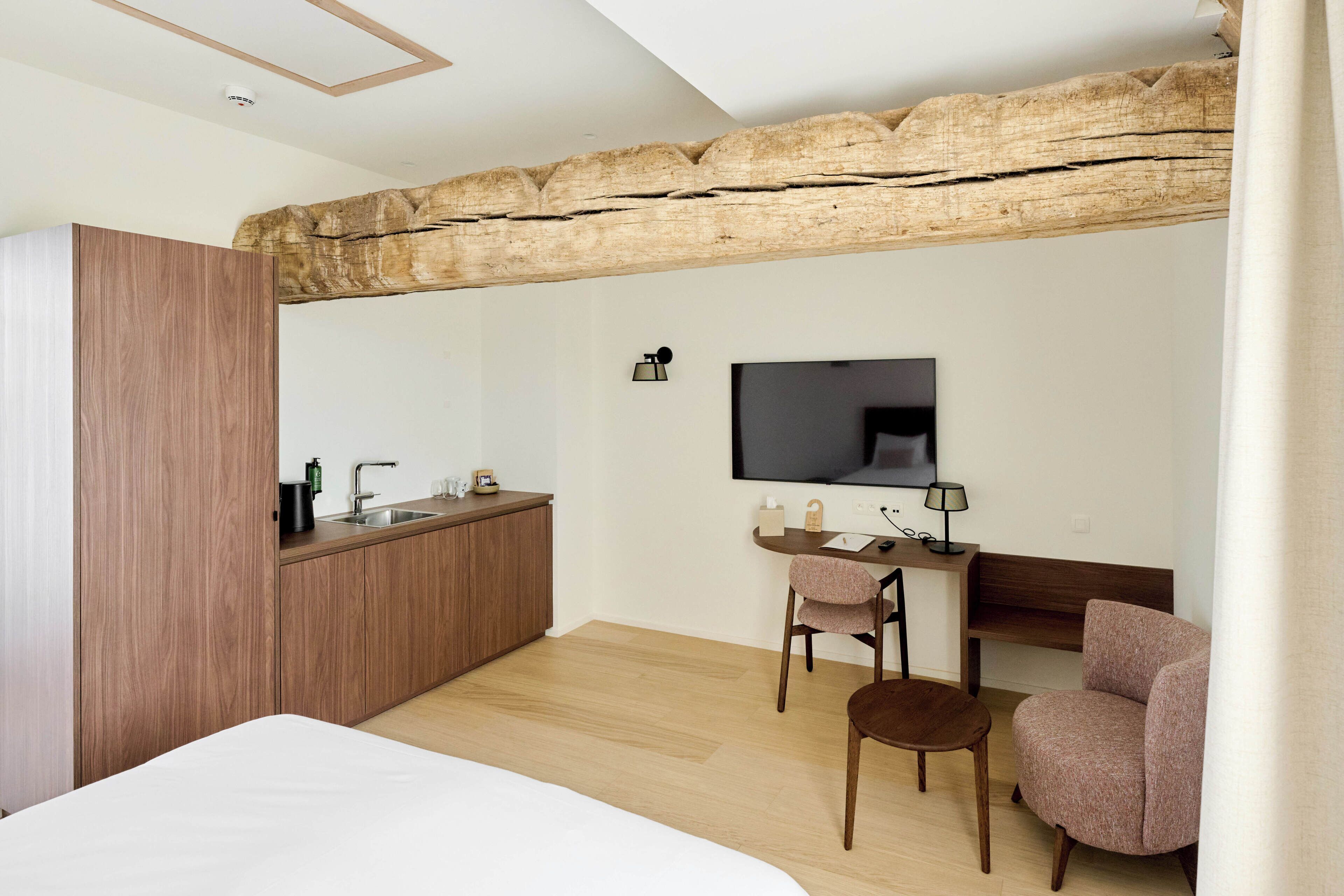 A modern hotel room with a wooden desk, a TV, a bed, and a chair.