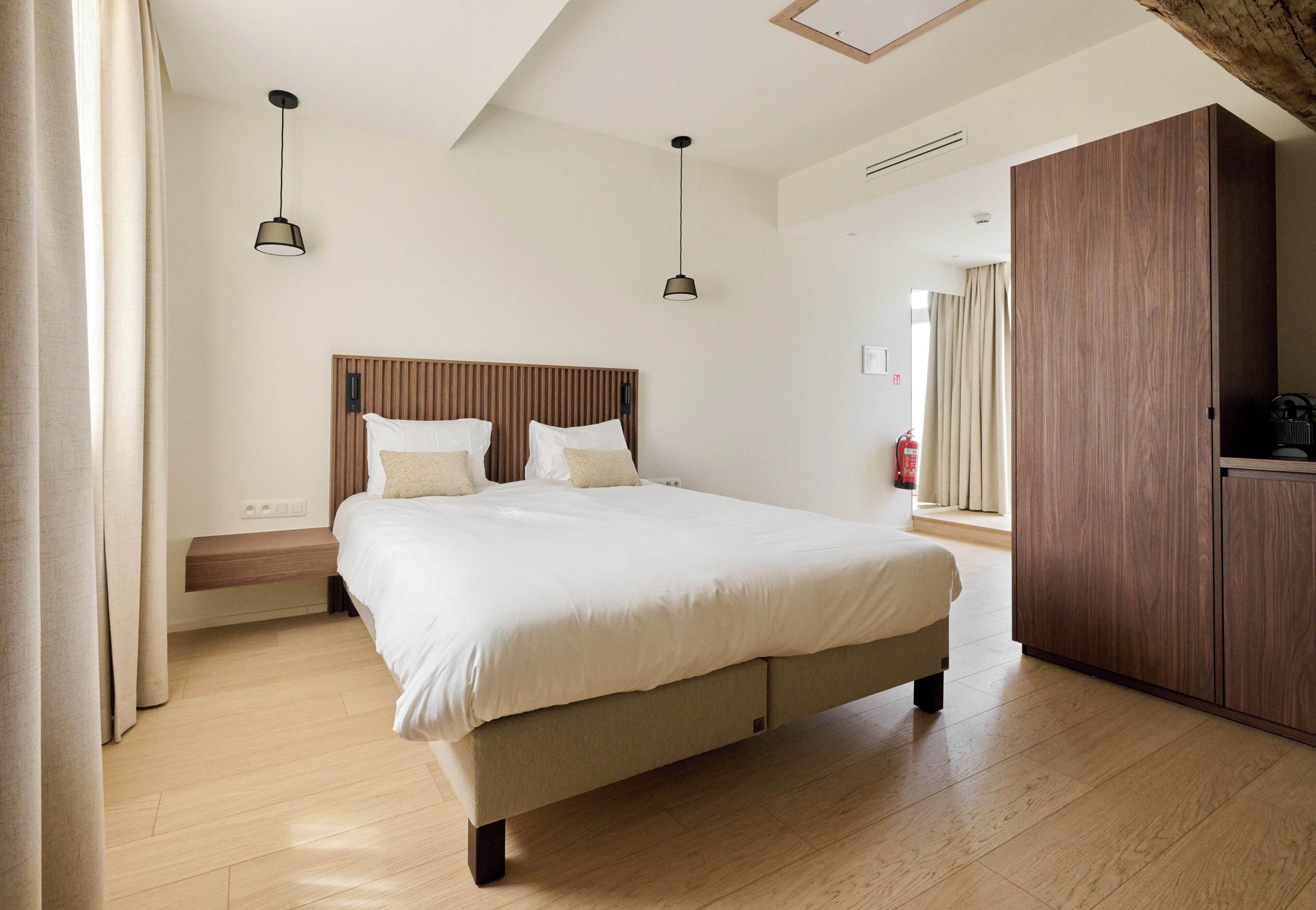 A bedroom with a large bed, wooden headboard, bedside tables, a wardrobe, and a ceiling light fixture.