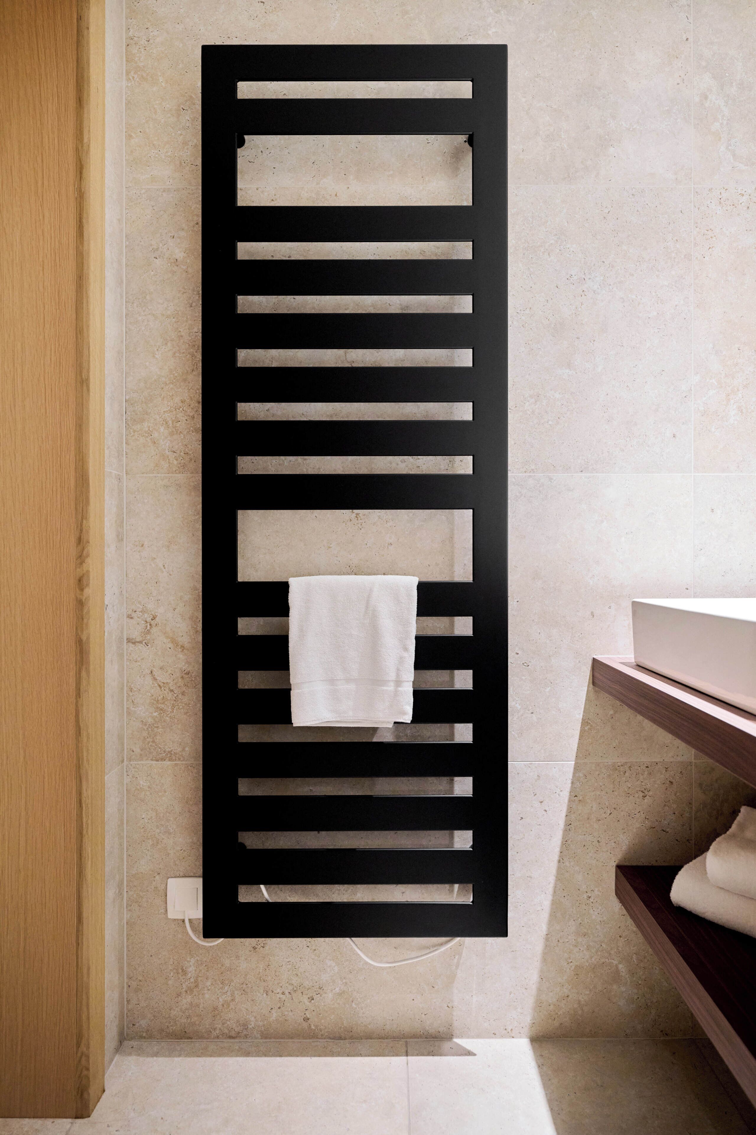 A black towel rack with a white towel hanging on it, mounted on a wall with a tiled floor.