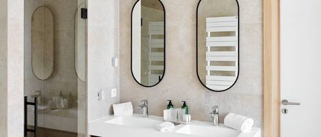 Un baño moderno con cabina de ducha de vidrio, tocador de madera y puerta blanca.