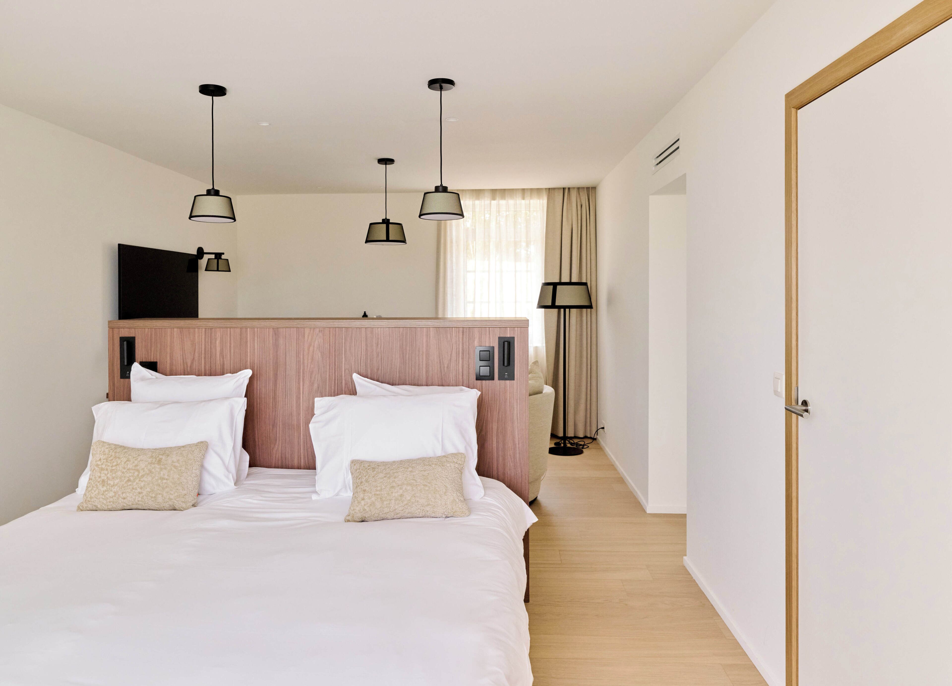 A hotel room with a bed, bedside lamps, a flat-screen TV, and a wooden headboard.