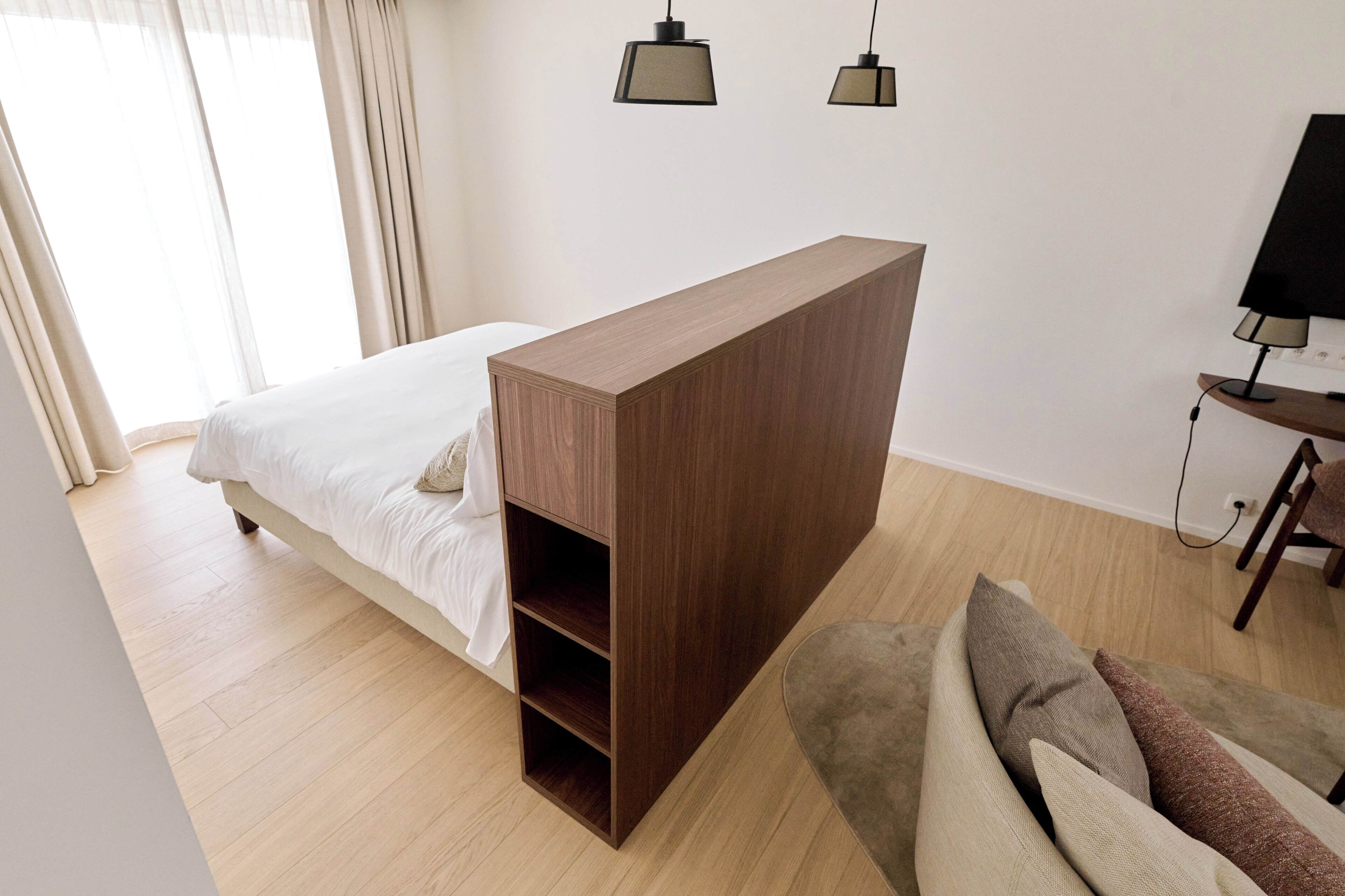 Een slaapkamer met een bed, een houten nachtkastje, een klein bureau met lamp en een bank.