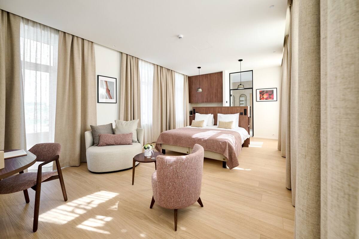 Une chambre d’hôtel moderne, équipée d’un lit, d’un canapé, d’un fauteuil et d’une petite table.