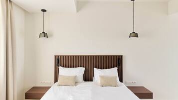 A modern bedroom with a wooden headboard, a large bed with white bedding, two bedside tables, and two pendant lights.