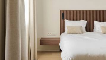 A bedroom with a bed, a bedside table, a hanging light fixture, and a window with curtains.