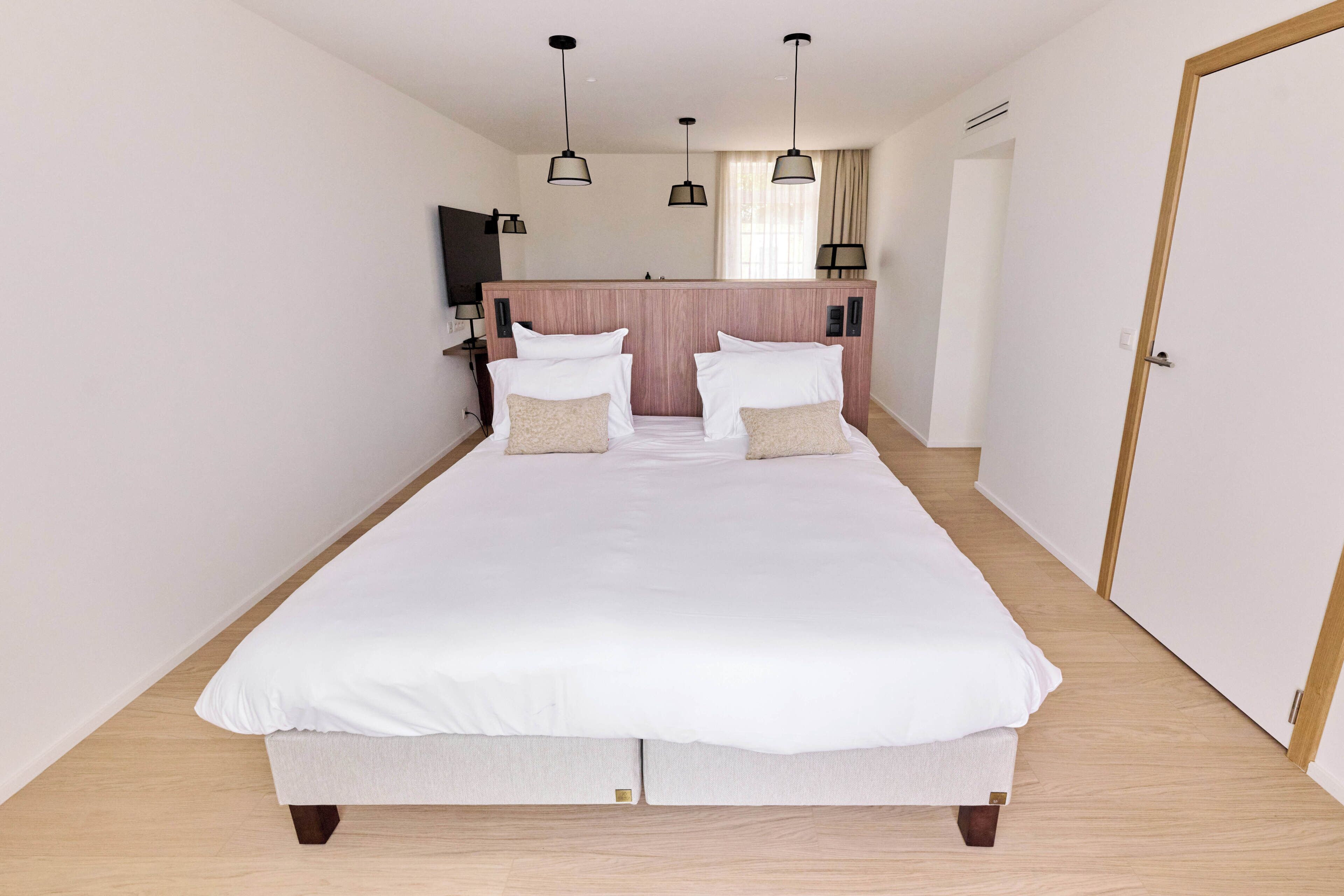 A neatly made double bed with white linens, a wooden headboard, and a bedside table with a lamp.