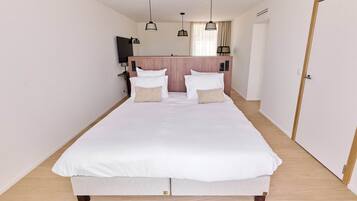 A neatly made double bed with white linens, a wooden headboard, and a bedside table with a lamp.