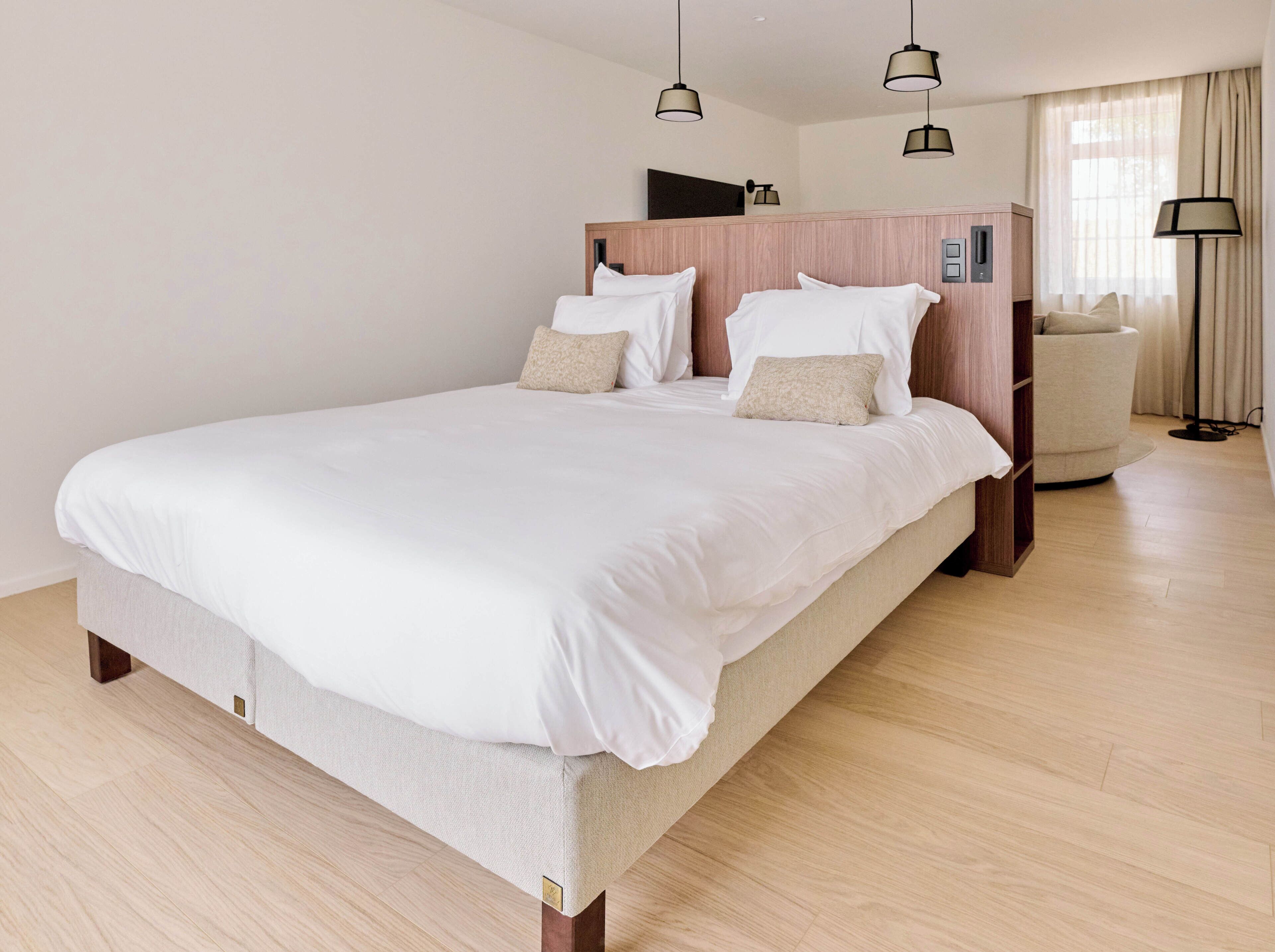A modern hotel room with a large bed, a bedside table, a chair, and a floor lamp.
