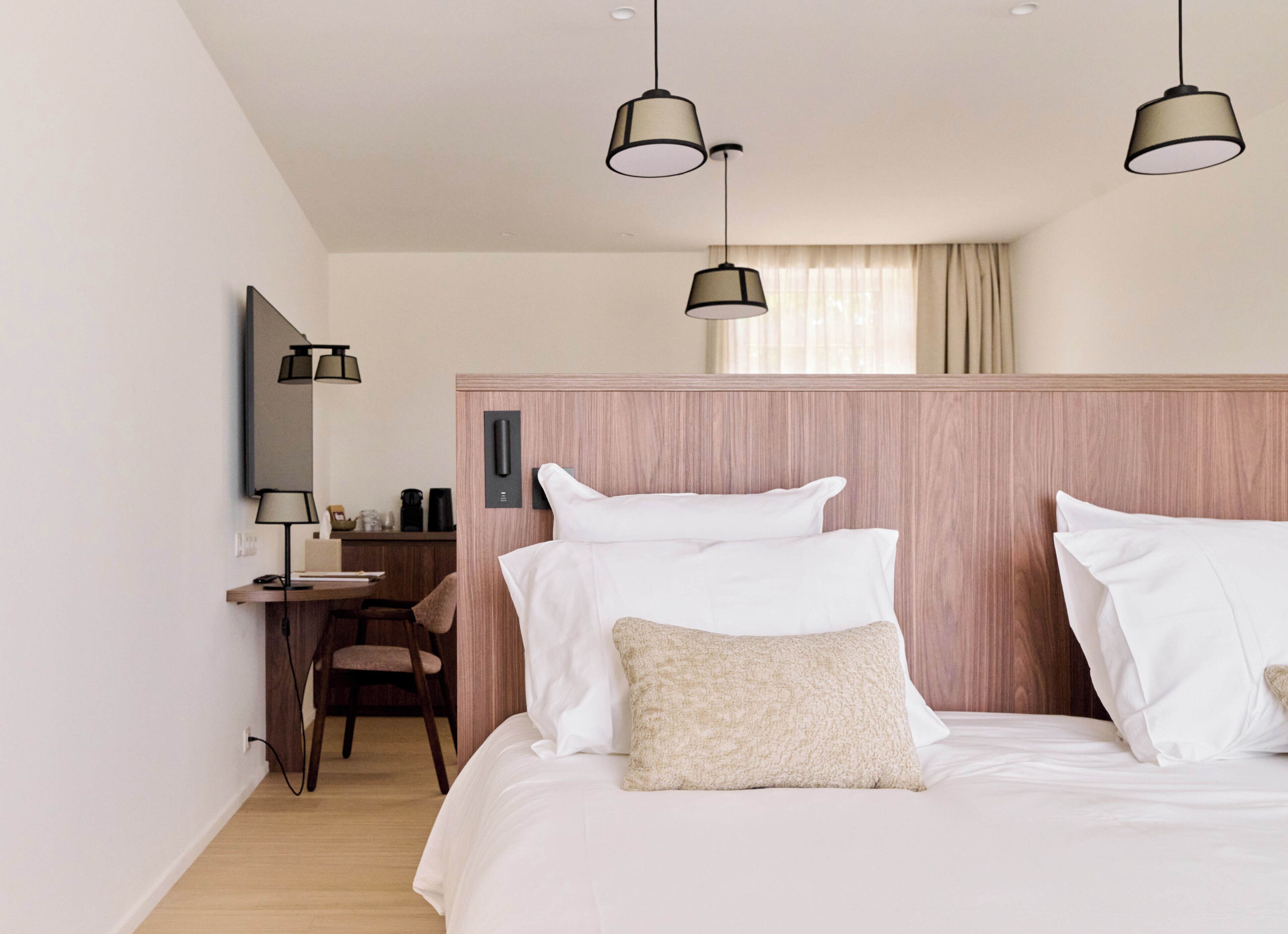 Una habitación de hotel con cama, mesita de noche, lámpara y escritorio con silla.