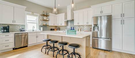 Una cocina moderna con armarios blancos, electrodomésticos de acero inoxidable y una isla central con taburetes.