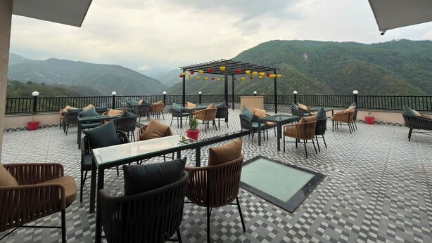 An outdoor seating area with tables and chairs, a pergola with colorful lanterns, and a mountainous backdrop.