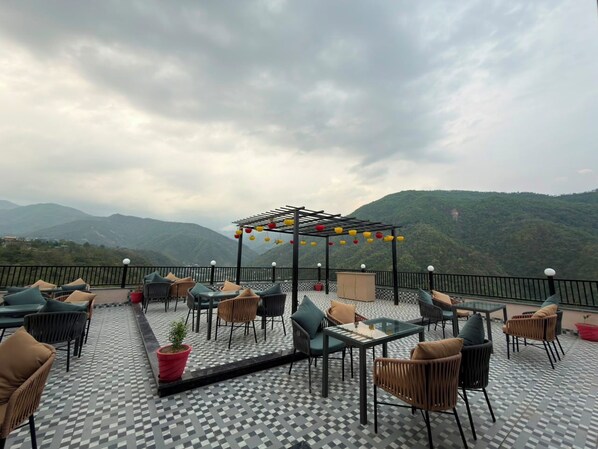Terraza exterior con asientos y pérgola, con vistas a un paisaje montañoso.