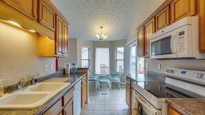A kitchen with wooden cabinets, a microwave, an oven, a sink, and a dining area with chairs. - 4 Mi to Ha Ha Tonka State Park! Home w/ Deck (Camdenton)