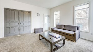 Ein Wohnzimmer mit grauem Sofa, Couchtisch, grauem Hocker und einer weißen Tür.