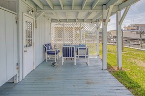 Eine überdachte Veranda mit Sitzgelegenheit, einer Tür und Blick auf Boote im Hintergrund.