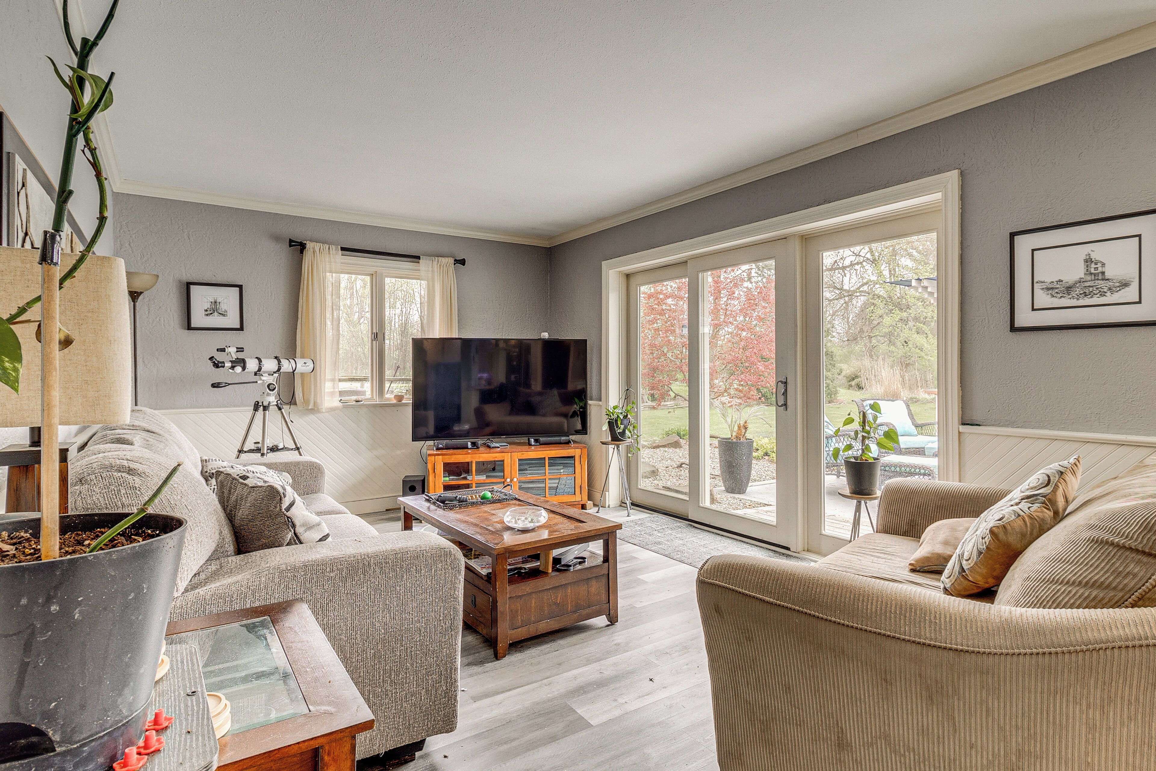 A living room with a sofa, coffee table, and a TV. There is a large window and a door leading outside.