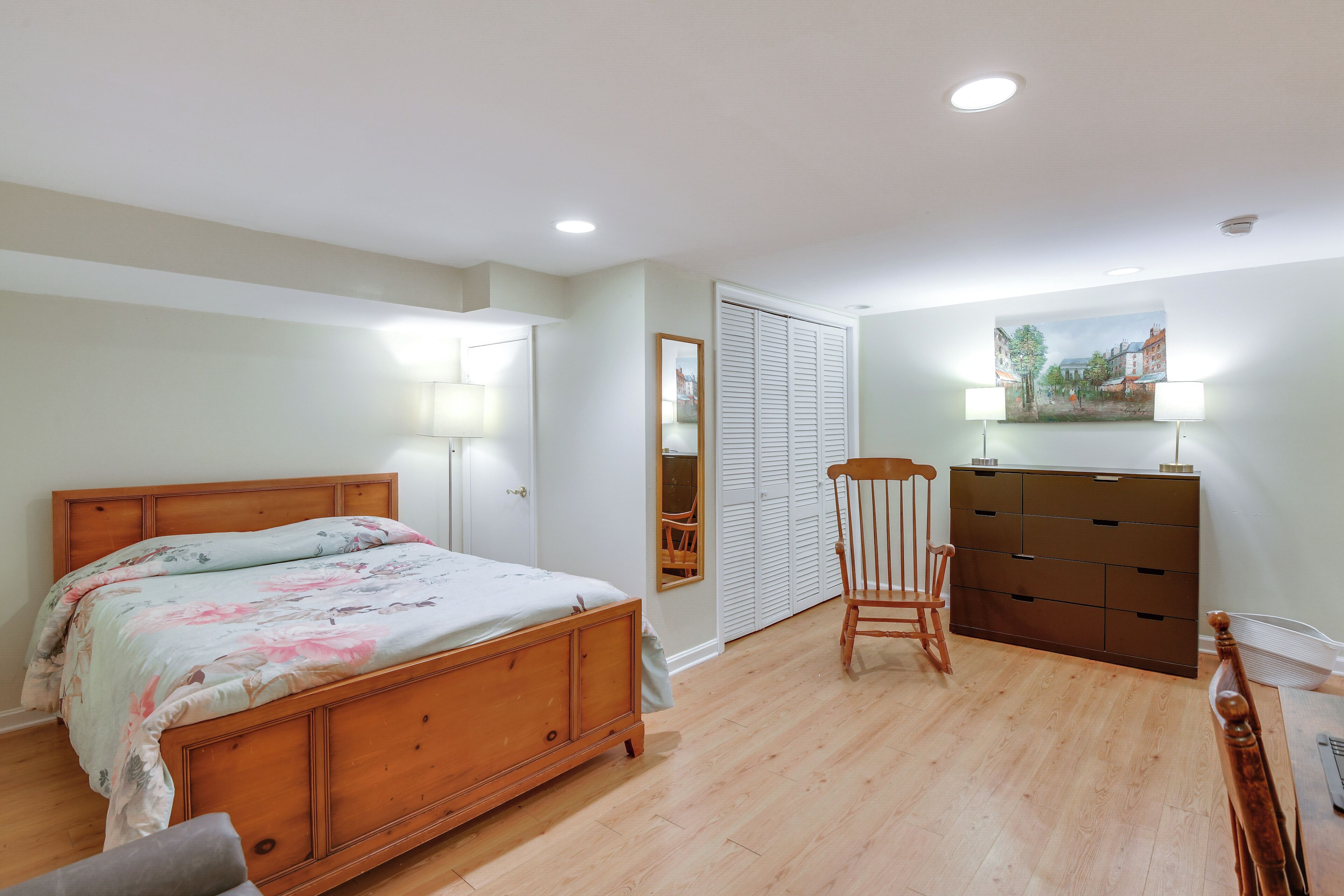 A bedroom with a wooden bed, a chair, a dresser, and a painting on the wall.