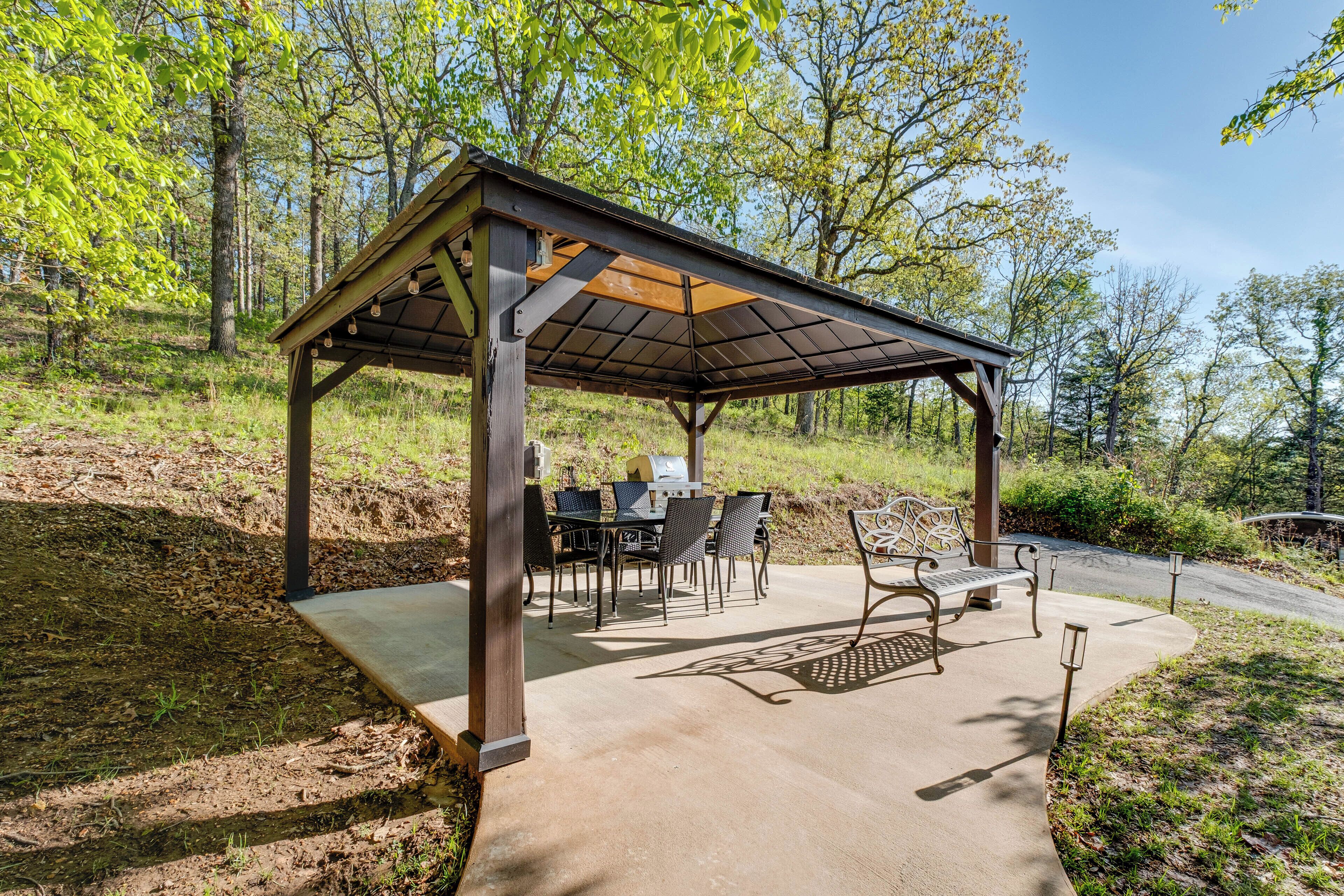 A covered outdoor seating area with tables and chairs, a grill, and a bench.