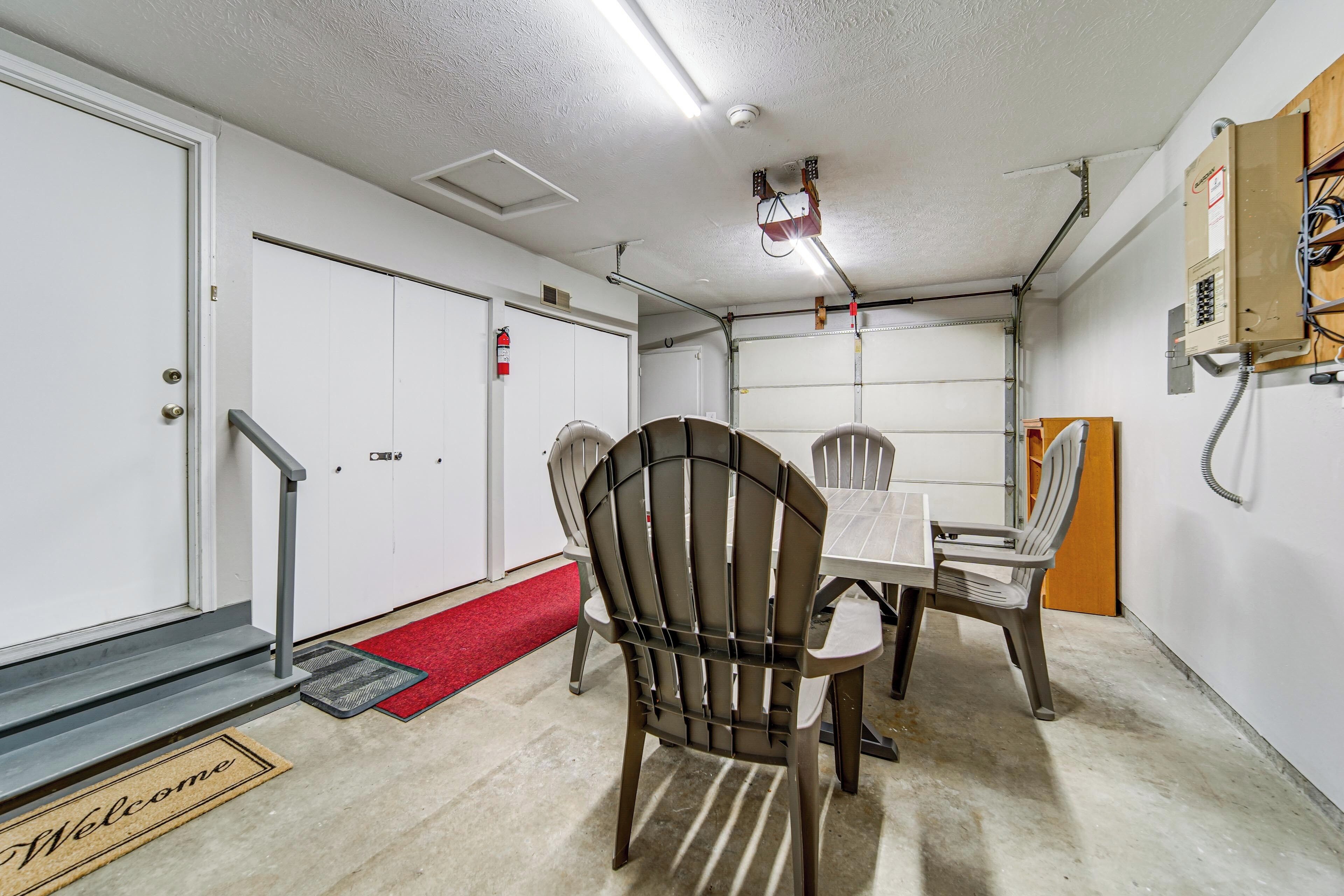 A room with a table, chairs, a red carpet, a welcome mat, a fire extinguisher, and a ceiling-mounted device.