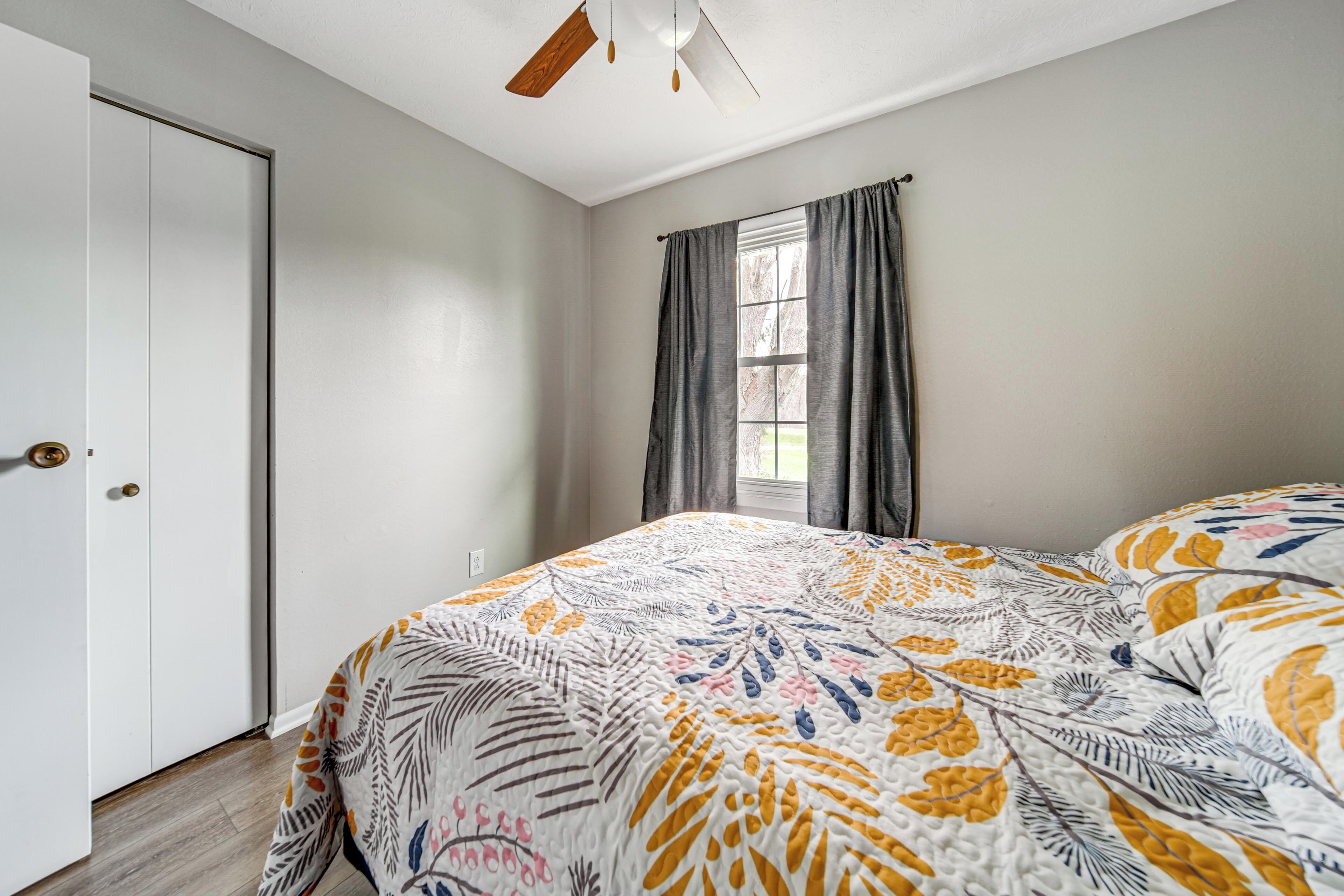 A bedroom with a bed, a window with curtains, a door, and a ceiling fan.