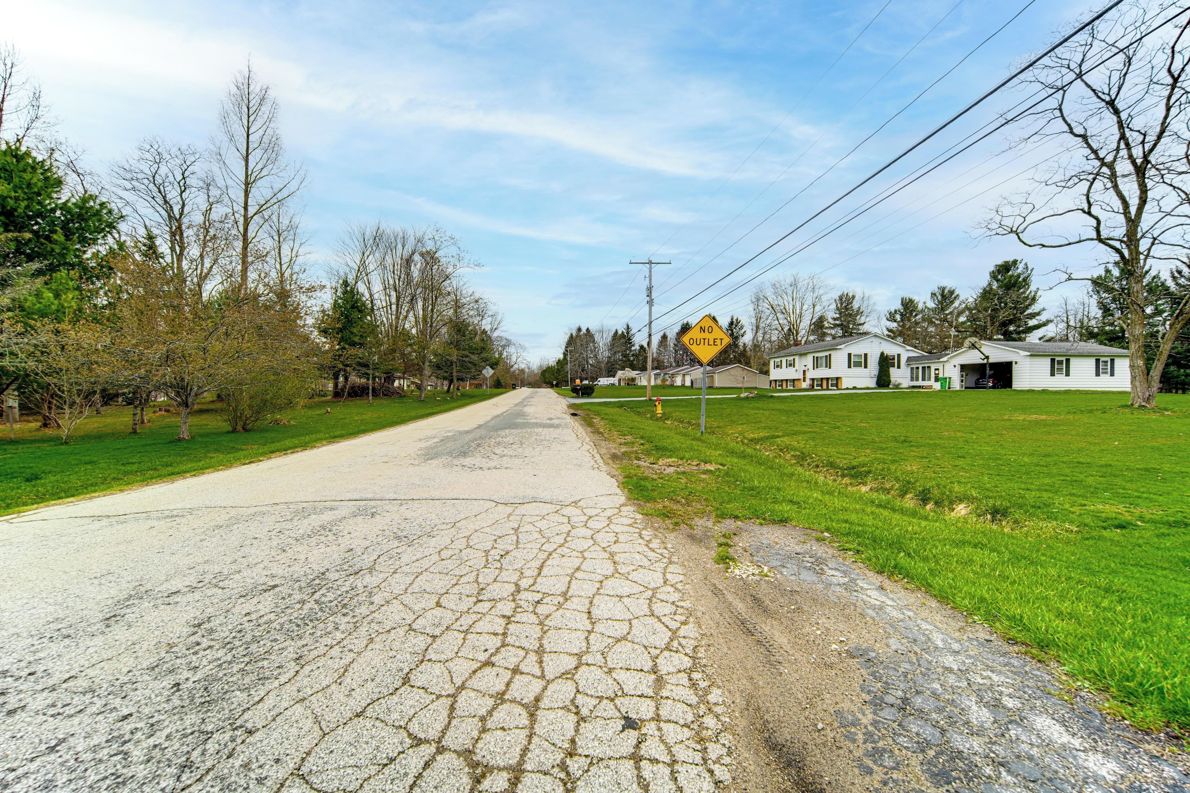 Un camino rural con un cartel de 'NO SALIDA', casas y un área verde.