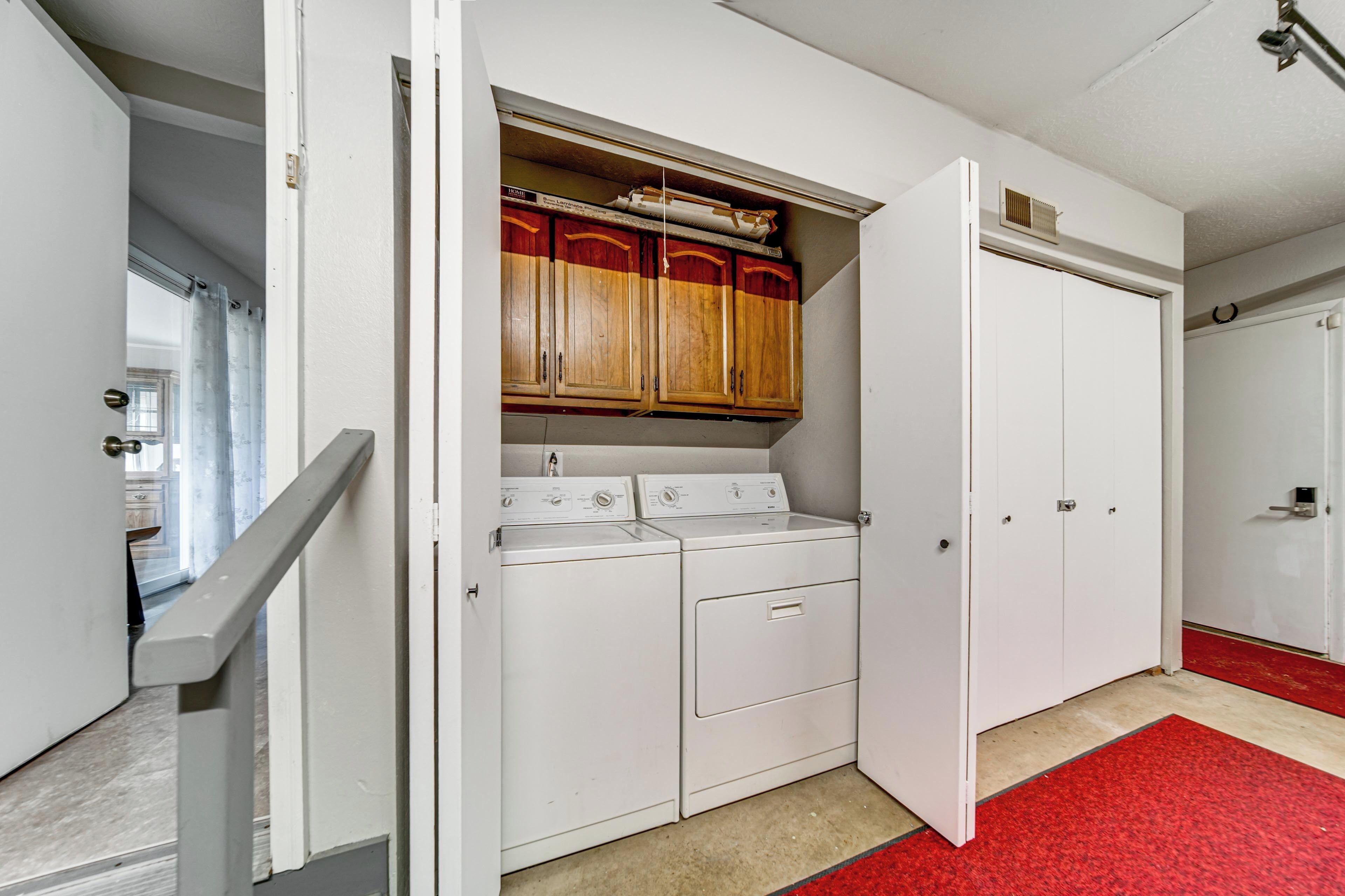A laundry room with a red carpet, wooden cabinets, and a white door.