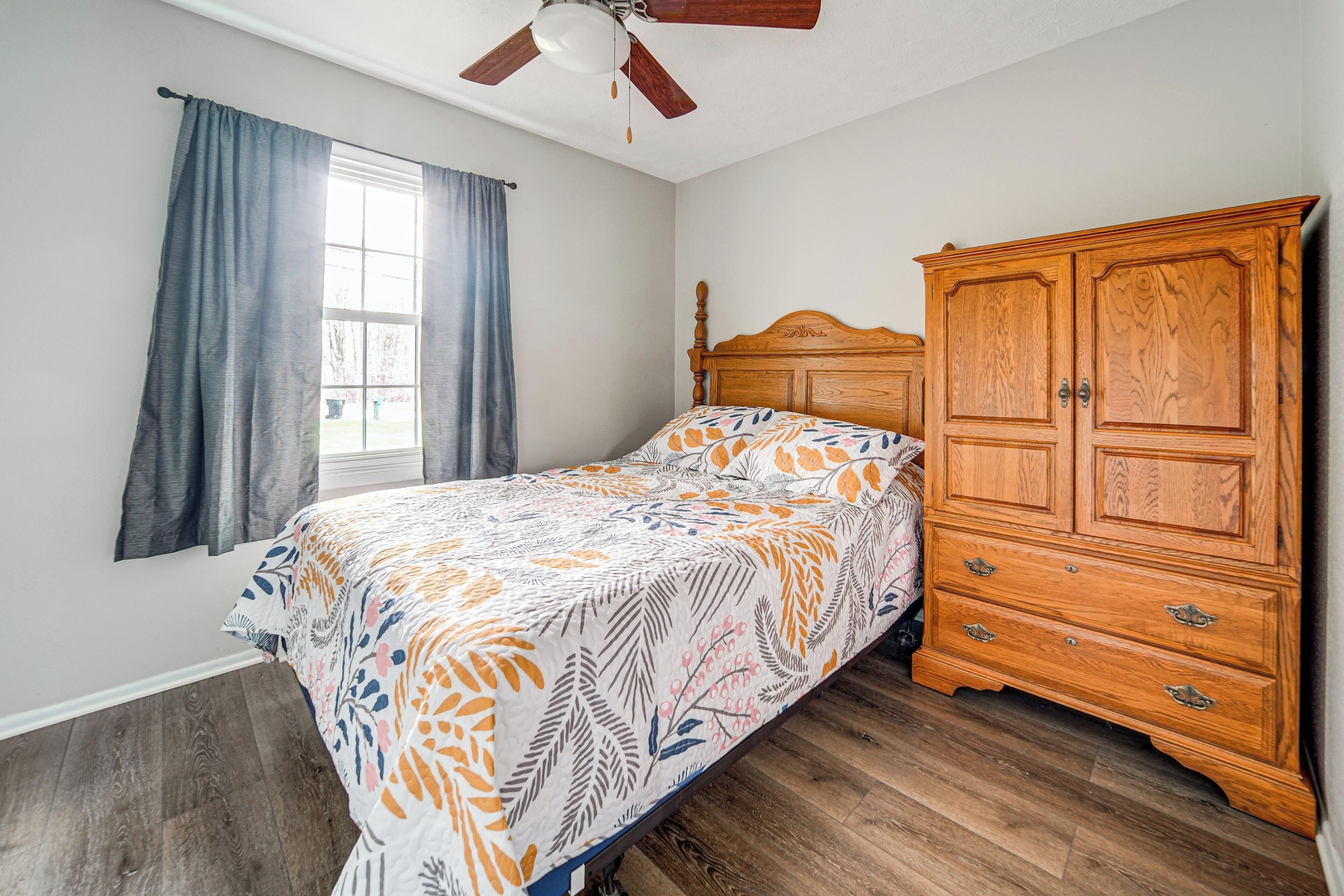 Ein Schlafzimmer mit Bett, Holzschrank, Fenster mit Vorhängen und Deckenventilator.
