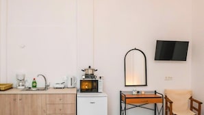 Ett litet kök med mikrovågsugn, kaffebryggare och vattenkokare. Det finns ett litet bord med en stol och en tv som är monterad på väggen.