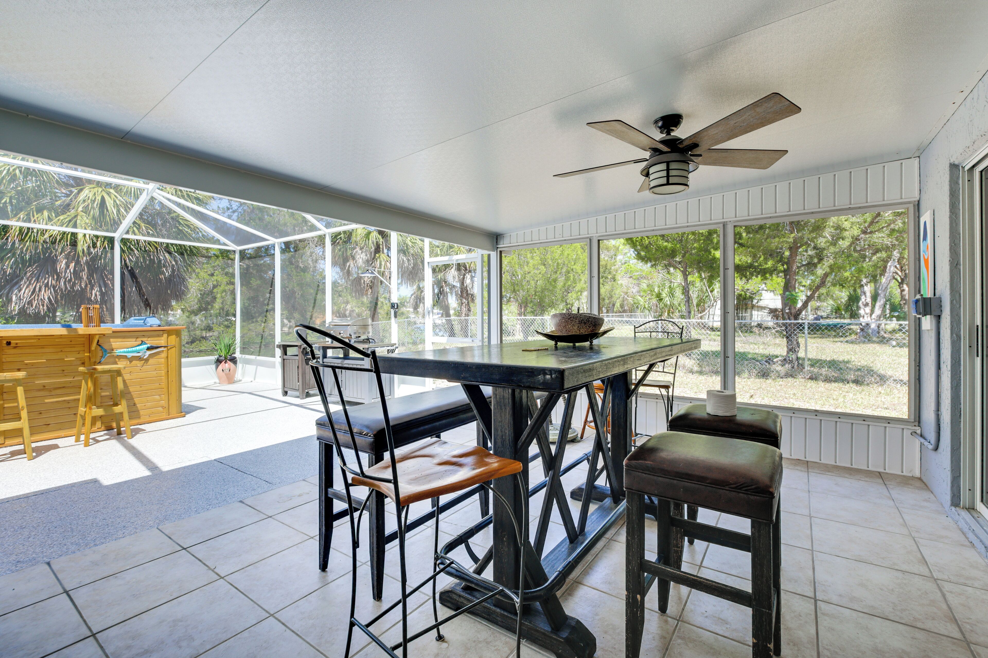 A covered patio with a table and chairs, a ceiling fan, and large windows offering a view of the outdoors.