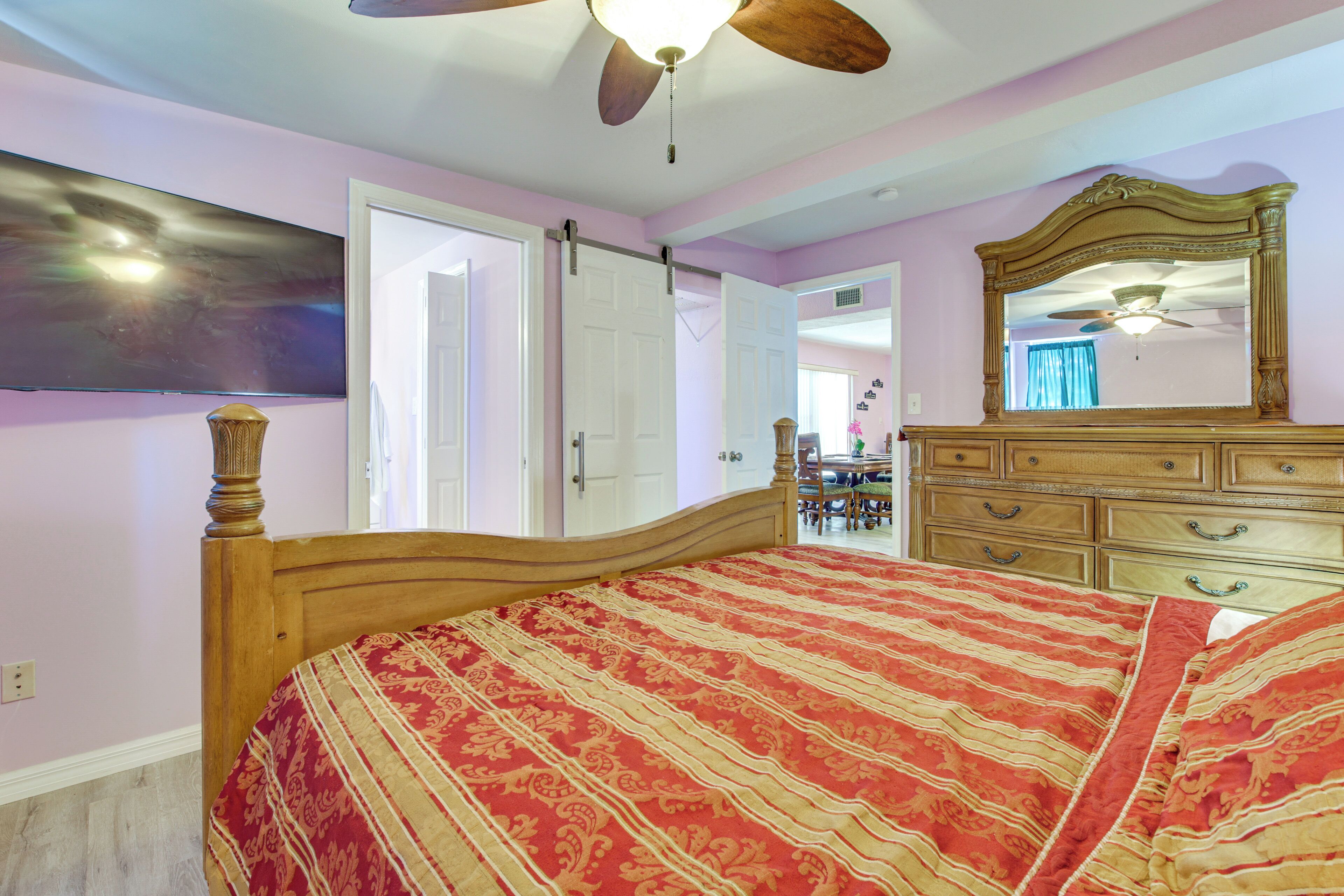 A bedroom with a wooden bed, a ceiling fan, a large mirror, and a door leading to another room.