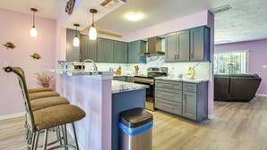 A modern kitchen with grey cabinets, a marble countertop, and a central island with bar stools. - Dockside Hernando Beach Retreat w/ Canal Access (Spring Hill)