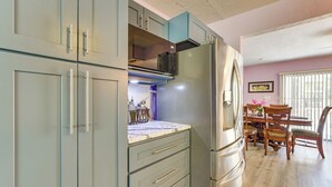 A kitchen with grey cabinets, a stainless steel refrigerator, and a dining area with wooden chairs and a table. - Dockside Hernando Beach Retreat w/ Canal Access (Spring Hill)