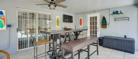 A dining area with a table, chairs, a bench, a ceiling fan, a television, and decorative items on the walls.